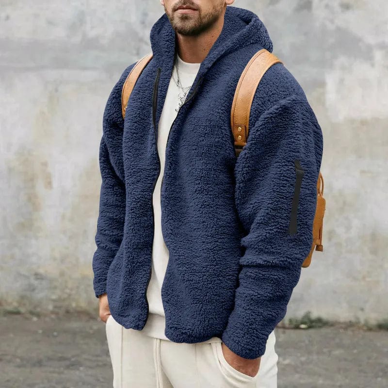 Uomo con giacca in pile blu, zaino marrone, sfondo grigio. Moda casual invernale, abbigliamento caldo, stile urbano.