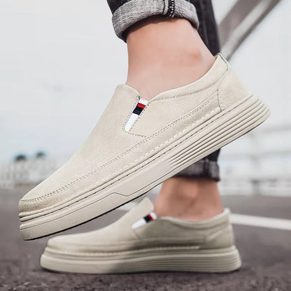 Scarpe slip-on beige da uomo su strada, design casual ed elegante, suola spessa, dettagli tricolore, perfette per moda urbana e comfort quotidiano.