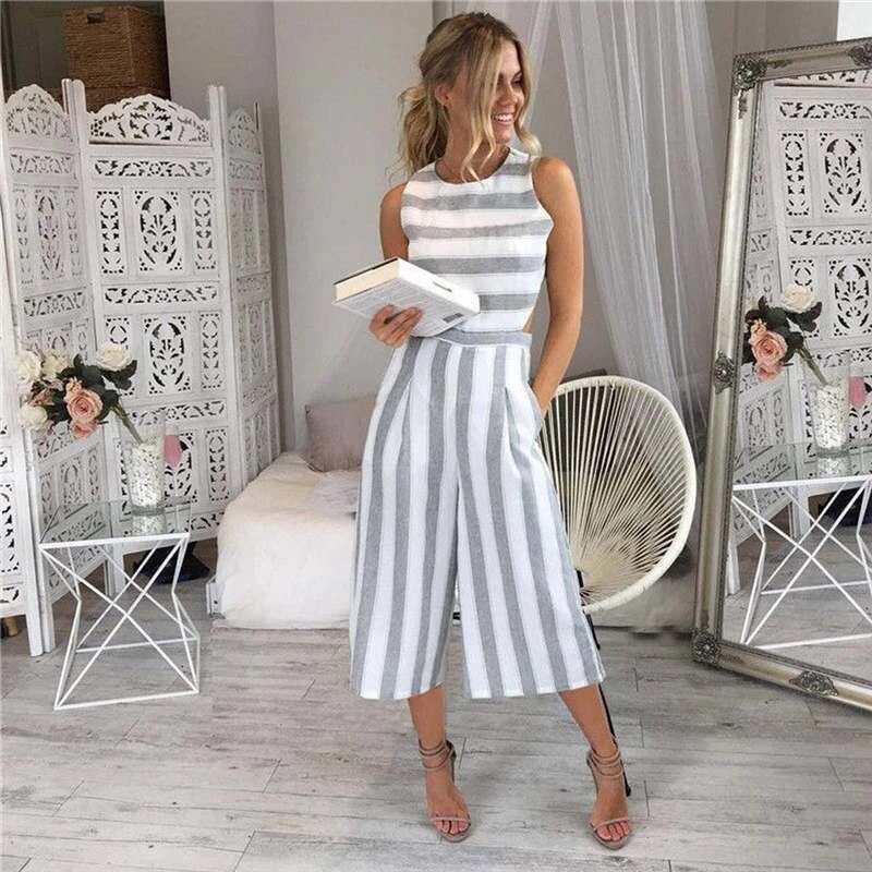 Donna in tuta a righe bianche e grigie, con libro in mano, in salotto elegante con decorazioni floreali e specchio. Moda estiva, abbigliamento casual.