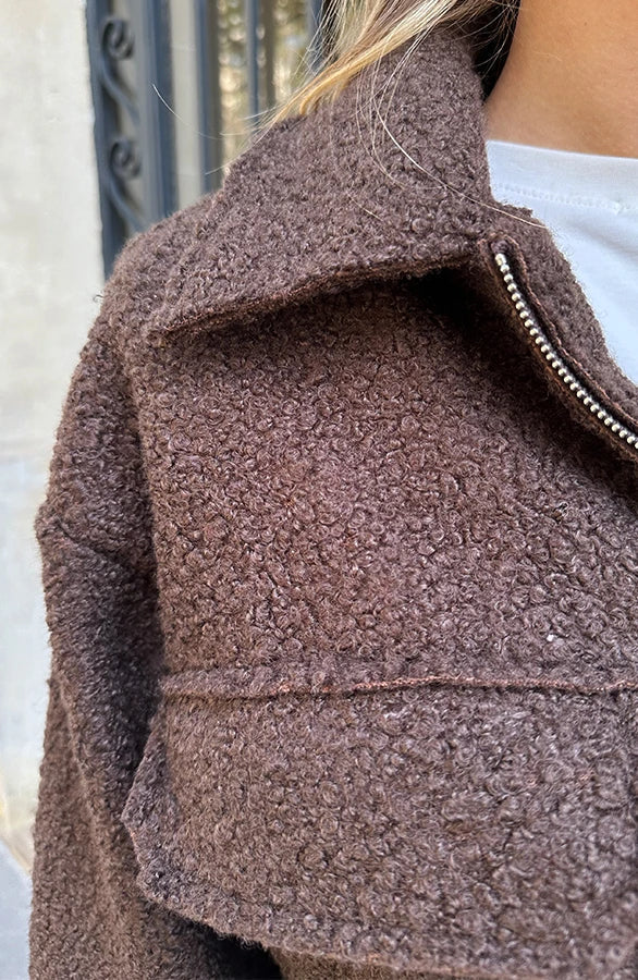 Giacca in lana bouclé marrone con cerniera, indossata da una persona. Tessuto caldo e strutturato, ideale per moda autunnale e invernale.
