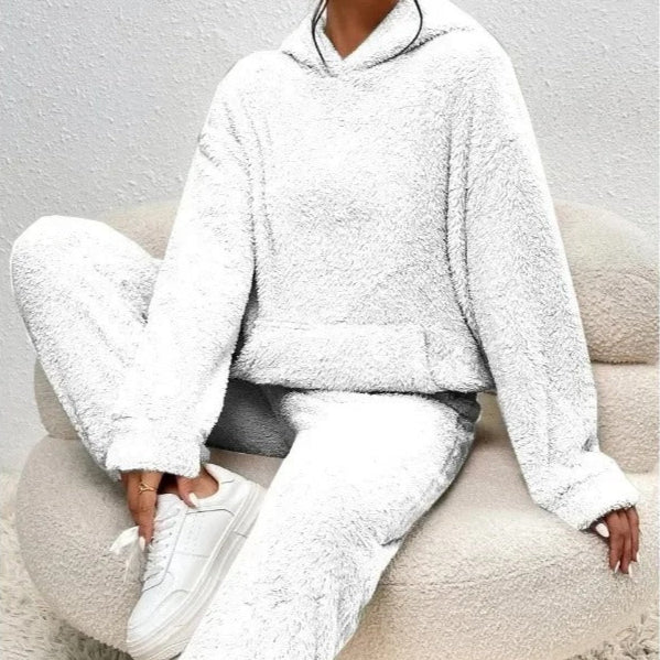 Donna seduta su poltrona indossa tuta bianca in pile, felpa con cappuccio e pantaloni abbinati. Moda comoda, abbigliamento casual, stile invernale.