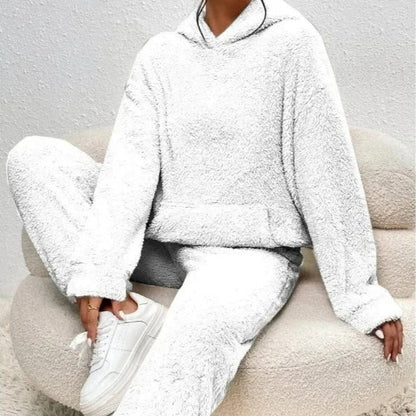 Donna seduta su poltrona indossa tuta bianca in pile, felpa con cappuccio e pantaloni abbinati. Moda comoda, abbigliamento casual, stile invernale.