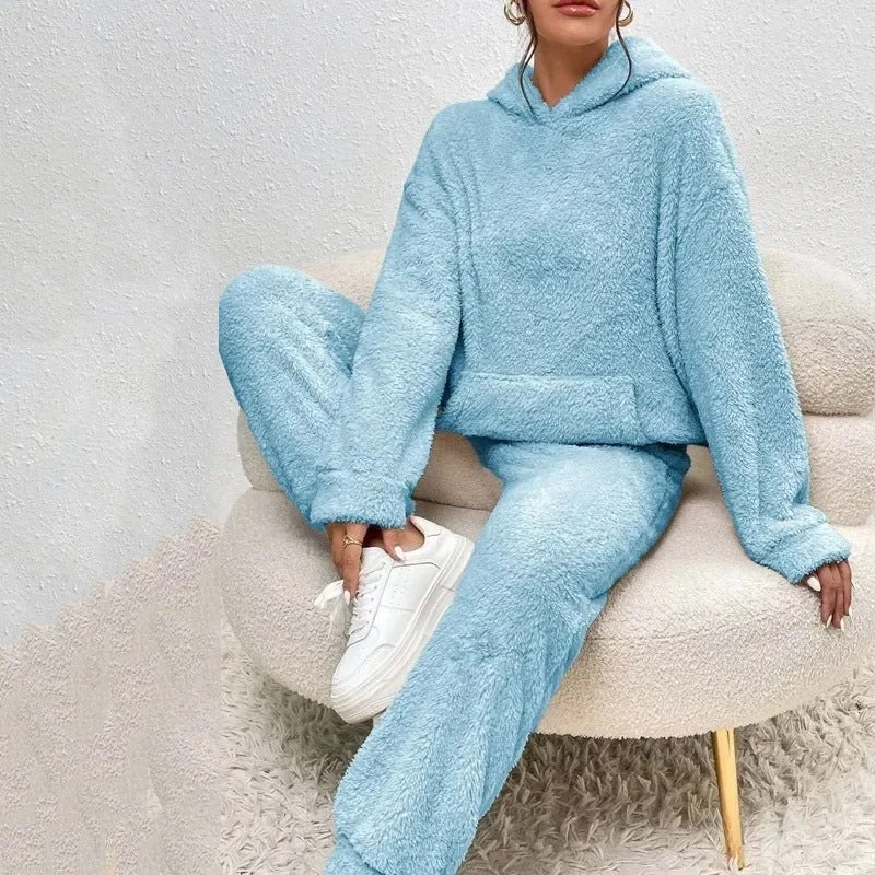Donna seduta su sedia indossa tuta felpata azzurra con cappuccio, abbinata a scarpe da ginnastica bianche. Look comodo e casual per l'inverno.