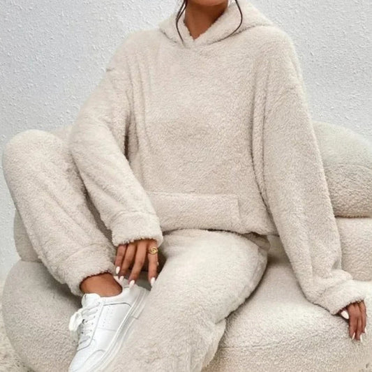 Donna seduta su poltrona indossa tuta in pile beige, comoda e calda, con cappuccio. Moda casual autunnale, abbigliamento loungewear trendy.