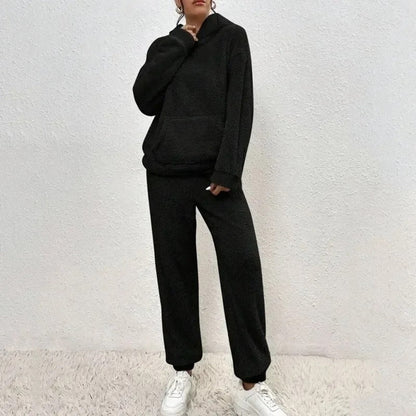 Donna in tuta sportiva nera, felpa con cappuccio e pantaloni, su sfondo bianco. Indossa scarpe da ginnastica bianche. Moda casual e comoda.