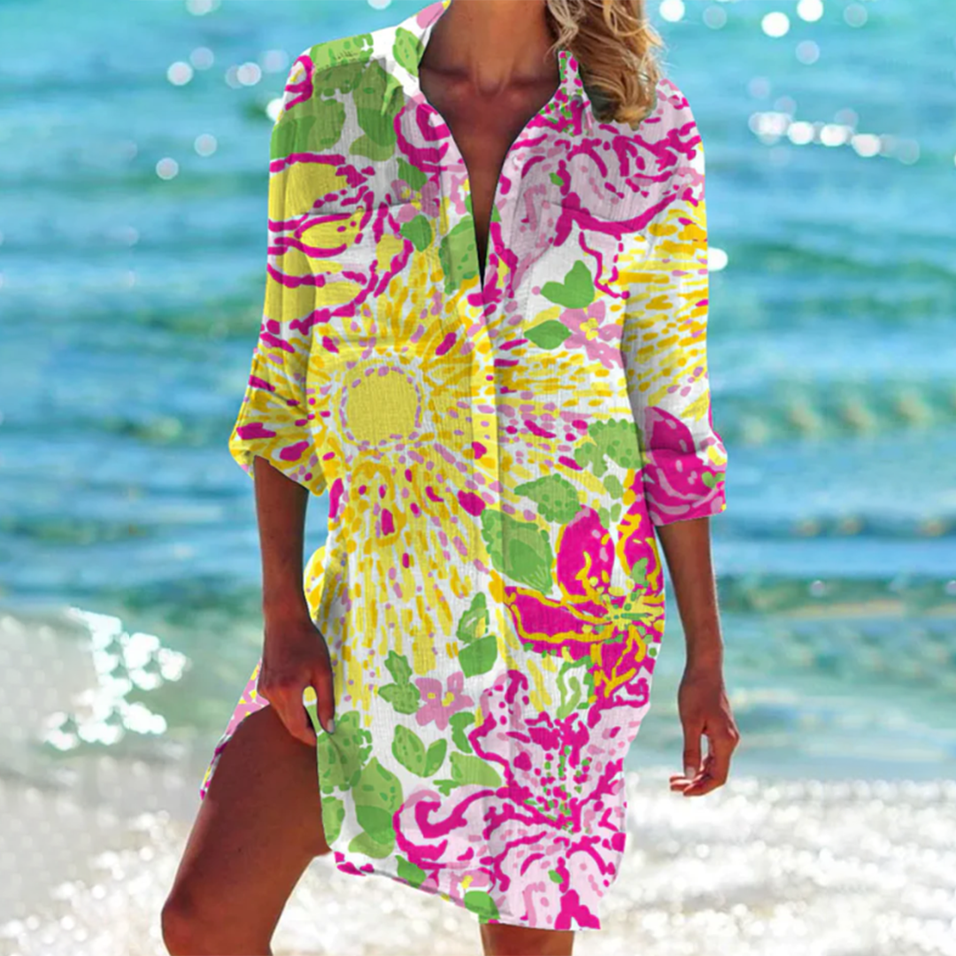 Donna in spiaggia con copricostume floreale colorato, sfondo mare azzurro. Moda estiva, abbigliamento mare, stile vacanza.