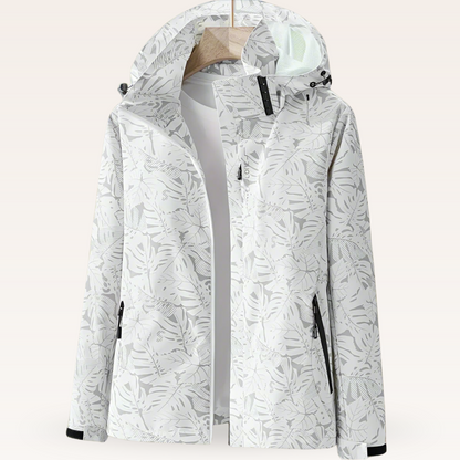 Giacca impermeabile bianca con cappuccio, motivo foglie grigie, chiusura zip, tasche laterali, ideale per outdoor e trekking.