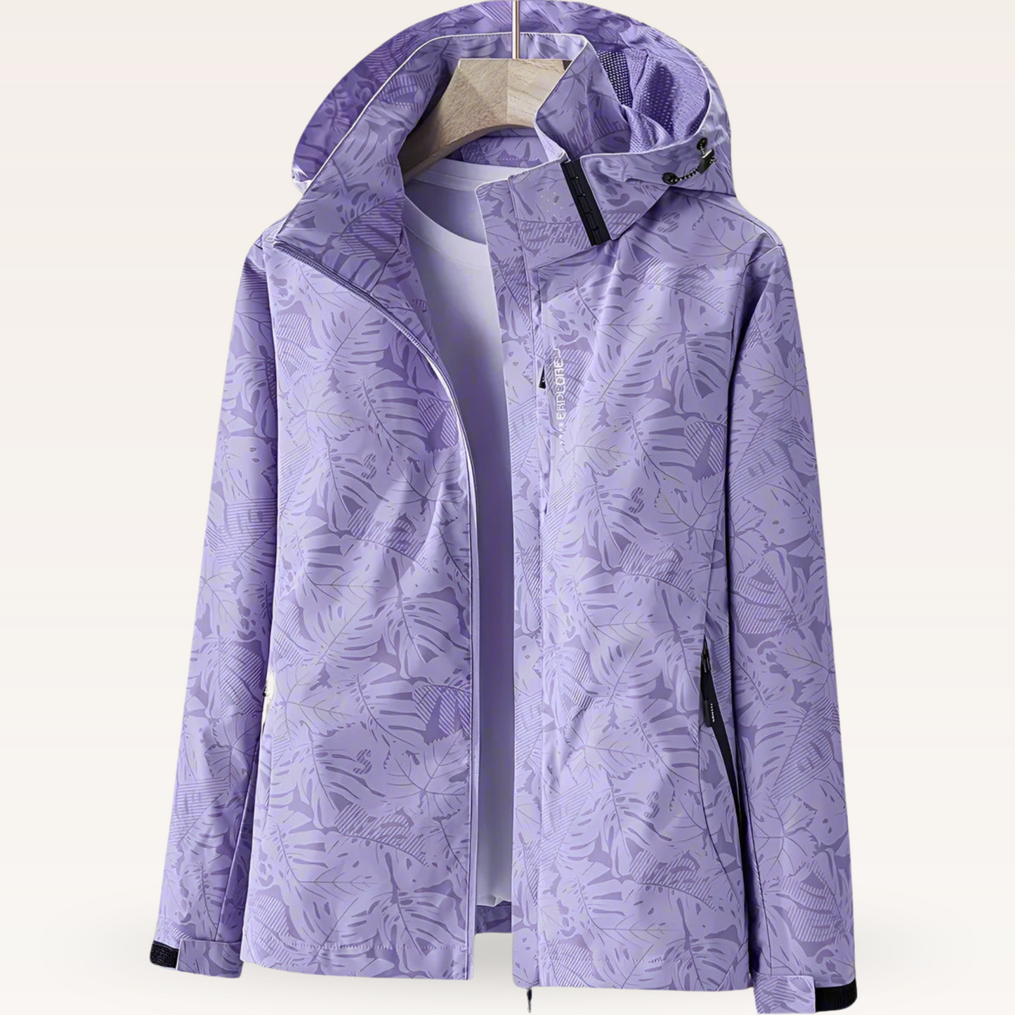 Giacca impermeabile viola con cappuccio, motivo foglie, appesa su gruccia. Abbigliamento outdoor, moda donna, tessuto tecnico resistente.
