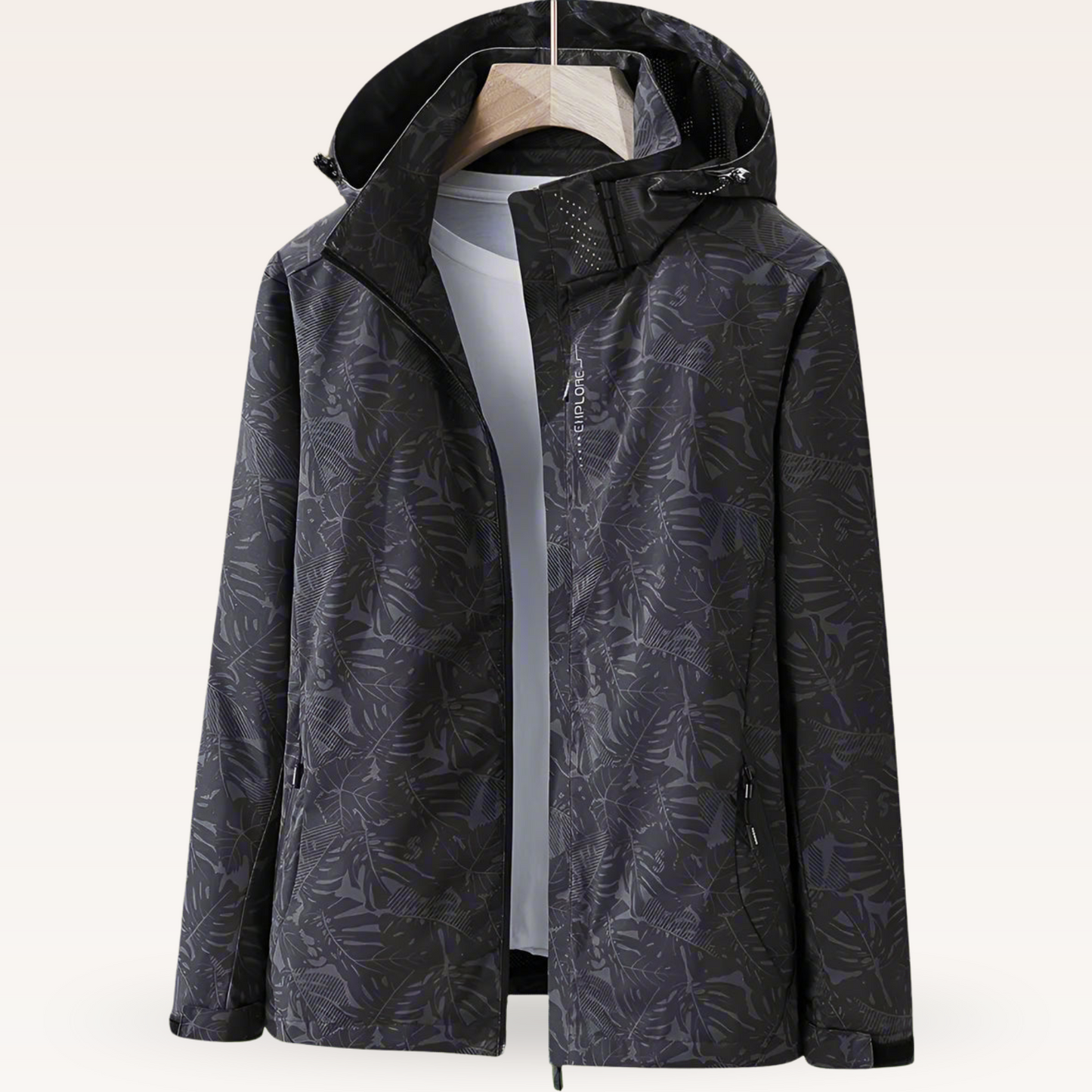 Giacca impermeabile nera con cappuccio, motivo foglie, appesa su gruccia. Abbigliamento outdoor, moda uomo, tessuto tecnico resistente.