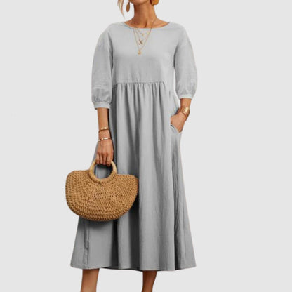 Abito lungo grigio con maniche a tre quarti, indossato con borsa di paglia intrecciata. Moda donna elegante, casual e chic.