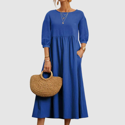 Abito lungo blu elegante con maniche a tre quarti, indossato con borsa di paglia intrecciata. Moda donna, abbigliamento estivo chic.