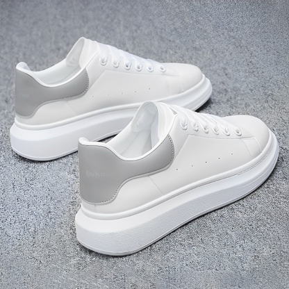 Scarpe da ginnastica bianche con suola spessa, dettagli grigi sul tallone, su sfondo grigio. Design moderno, calzature casual eleganti.