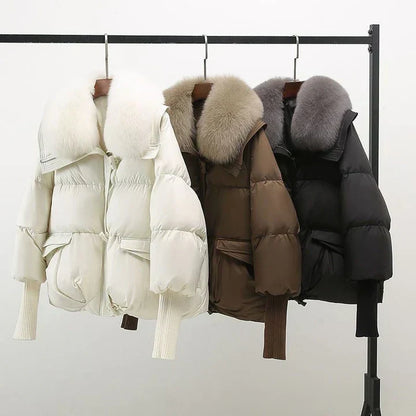 Giacche invernali imbottite con cappuccio in pelliccia sintetica, colori bianco, marrone e nero, appese su un appendiabiti. Moda donna, abbigliamento caldo.