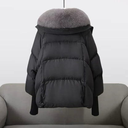 Giacca invernale nera con collo in pelliccia grigia, design imbottito, appesa su sfondo chiaro. Moda donna, abbigliamento caldo, stile elegante.
