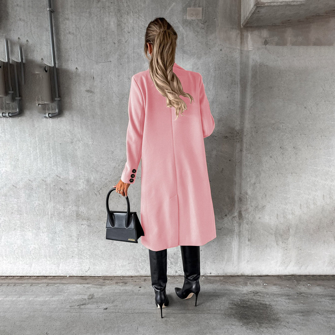 Donna di spalle con cappotto rosa, borsa nera e stivali alti, in un ambiente industriale. Moda autunnale, stile elegante, tendenze 2023.
