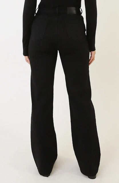 Donna in jeans neri a zampa, vista posteriore. Moda casual, pantaloni a vita alta, stile anni '70. Abbigliamento femminile trendy e moderno.