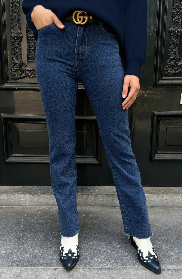 Jeans blu leopardati, cintura nera con fibbia dorata, stivali bianchi e neri, porta nera decorata. Moda urbana, stile casual chic.