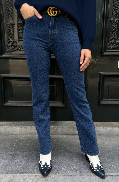 Jeans blu leopardati, cintura nera con fibbia dorata, stivali bianchi e neri, porta nera decorata. Moda urbana, stile casual chic.