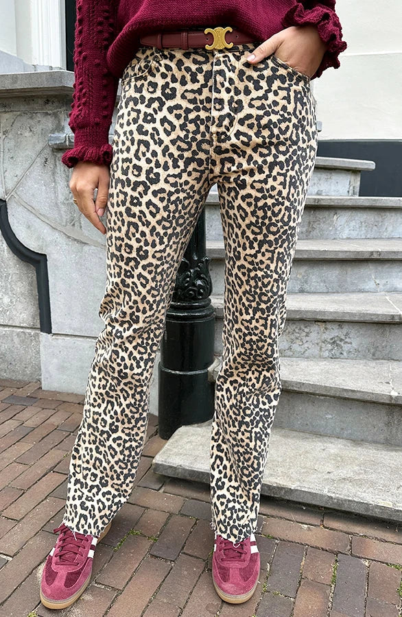 Pantaloni leopardati donna, moda autunno, abbinati a maglione rosso e scarpe sportive rosa, stile casual urbano su sfondo di scale in pietra.