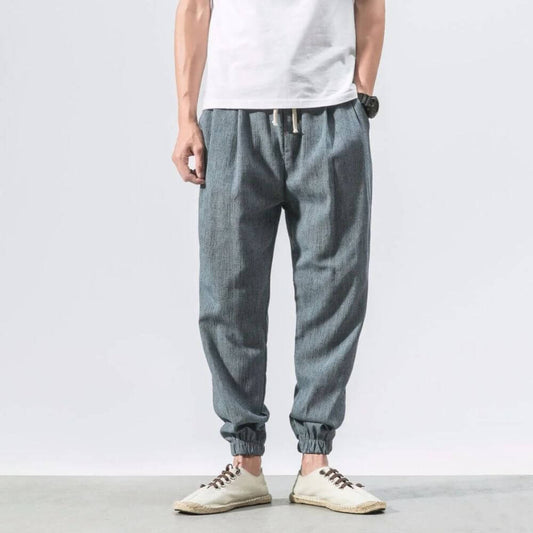 Uomo in pantaloni jogger grigi, casual e comodi, con elastico alla caviglia, abbinati a scarpe bianche e maglietta bianca. Moda maschile casual.
