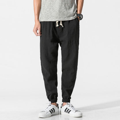 Pantaloni jogger neri da uomo, tessuto leggero, abbinati a scarpe da ginnastica bianche e maglietta grigia. Stile casual e moderno.