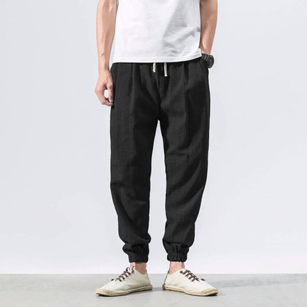Pantaloni jogger neri da uomo in lino, abbinati a una maglietta bianca e scarpe casual. Stile casual, moda maschile, abbigliamento estivo.