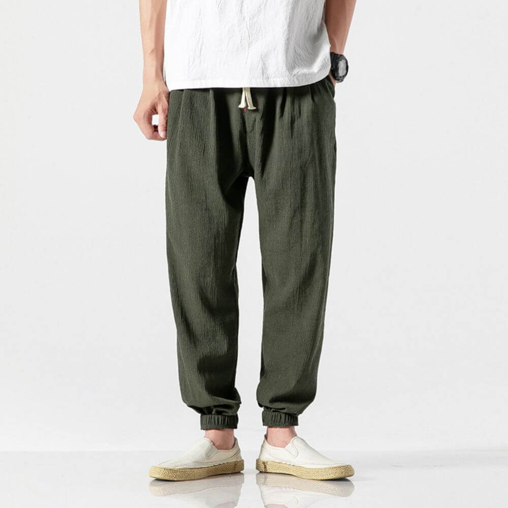Pantaloni jogger verde oliva da uomo, tessuto leggero, elastico in vita con laccio, abbinati a scarpe casual beige e maglietta bianca.