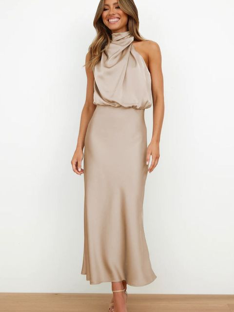 Donna in abito lungo beige elegante, senza maniche, con collo alto drappeggiato. Moda femminile, abbigliamento da sera, stile sofisticato.