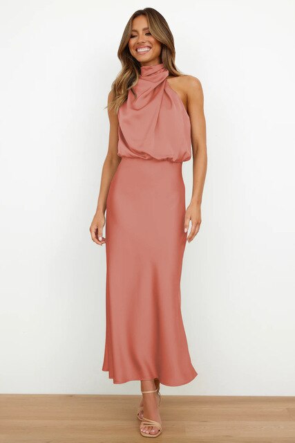 Donna in abito lungo rosa salmone, senza maniche, con scollo all'americana, su sfondo bianco. Moda elegante, abbigliamento femminile chic.