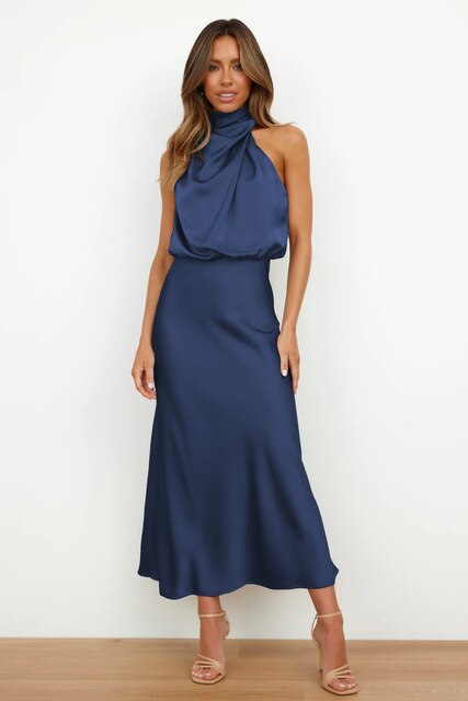 Donna con abito lungo blu satinato, senza maniche e collo alto, posa su sfondo bianco. Moda elegante, abbigliamento femminile, stile sofisticato.