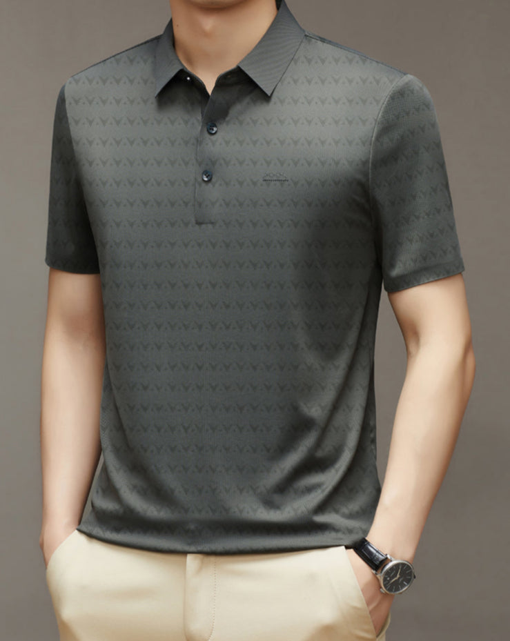Uomo con polo grigia a maniche corte, motivo geometrico, indossa pantaloni beige e orologio nero. Moda casual elegante maschile.