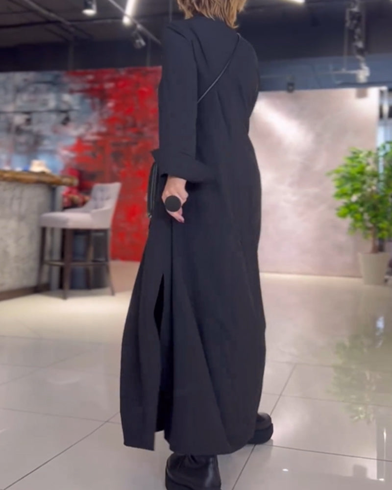 Donna in abito lungo nero elegante, con microfono in mano, cammina su pavimento lucido. Sfondo con parete rossa e pianta verde. Moda moderna.