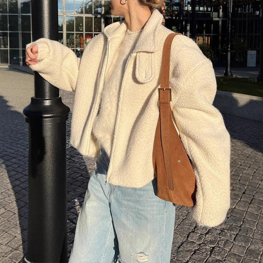 Donna con giacca di lana bianca, jeans strappati e borsa a tracolla marrone, cammina all'aperto in una giornata soleggiata. Moda autunnale casual.
