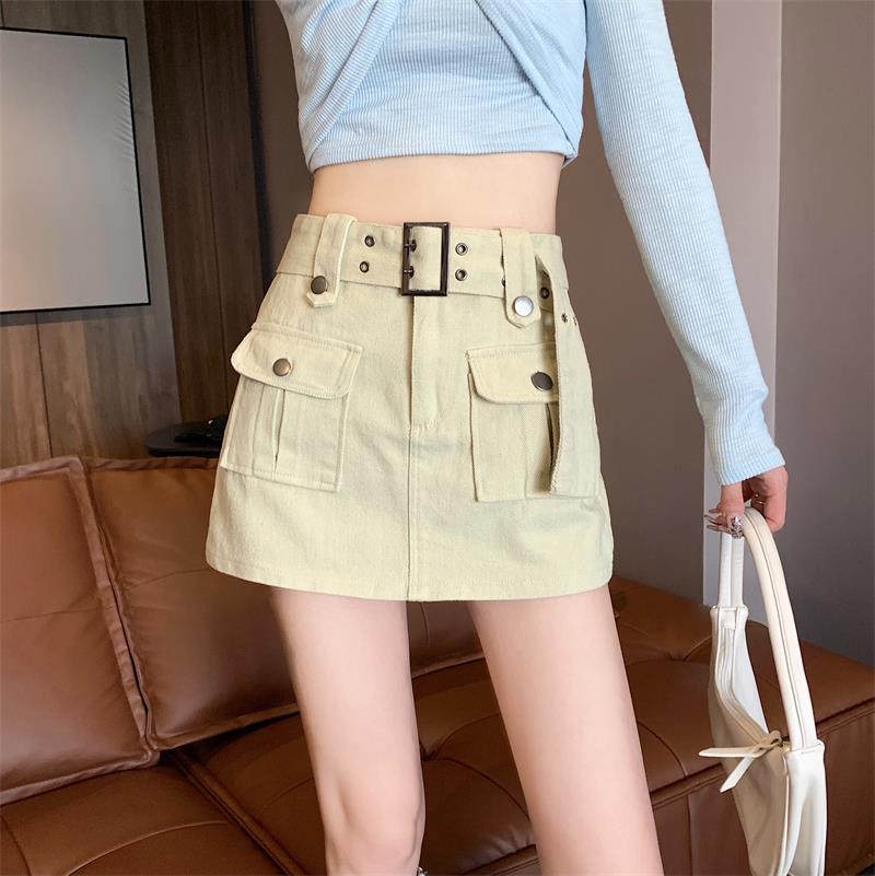 Minigonna beige con tasche e cintura, indossata da una persona con maglia azzurra, su divano marrone. Moda femminile, abbigliamento casual chic.