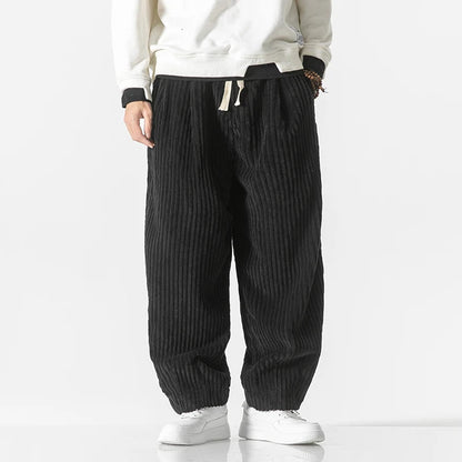Pantaloni larghi a coste nere, indossati con felpa bianca e scarpe da ginnastica bianche. Stile casual, moda uomo, abbigliamento comodo.