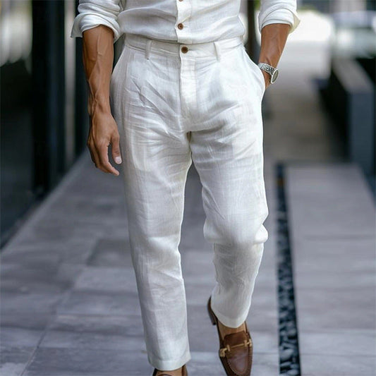 Uomo in abito di lino bianco, camicia e pantaloni eleganti, cammina su marciapiede. Moda estiva maschile, stile casual chic, scarpe marroni.