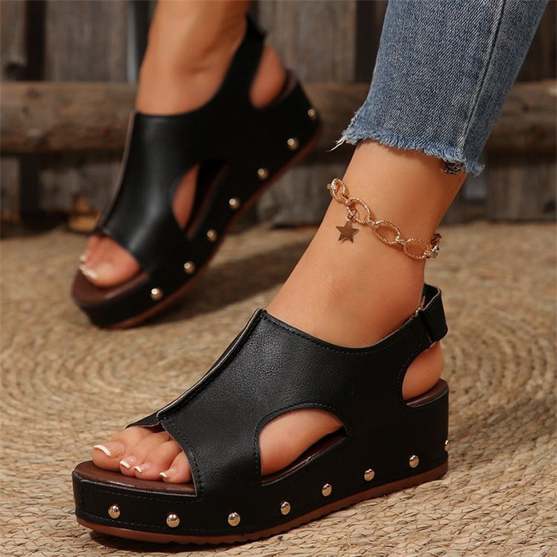 Sandali neri con zeppa e borchie, indossati con jeans strappati e cavigliera dorata a stella. Scarpe estive eleganti e alla moda.