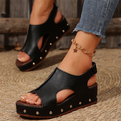 Sandali neri con zeppa e borchie, indossati con jeans strappati e cavigliera dorata a stella. Scarpe estive eleganti e alla moda.