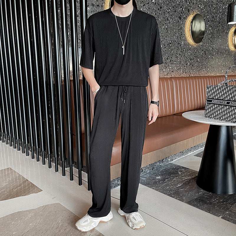 Uomo in abbigliamento casual nero, con pantaloni e maglietta, in un moderno caffè con pareti scure e arredamento elegante.