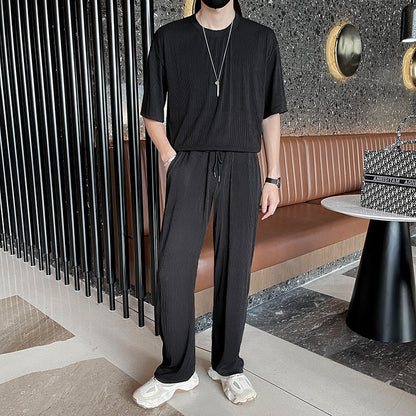 Uomo in abbigliamento casual nero, con pantaloni e maglietta, in un moderno caffè con pareti scure e arredamento elegante.