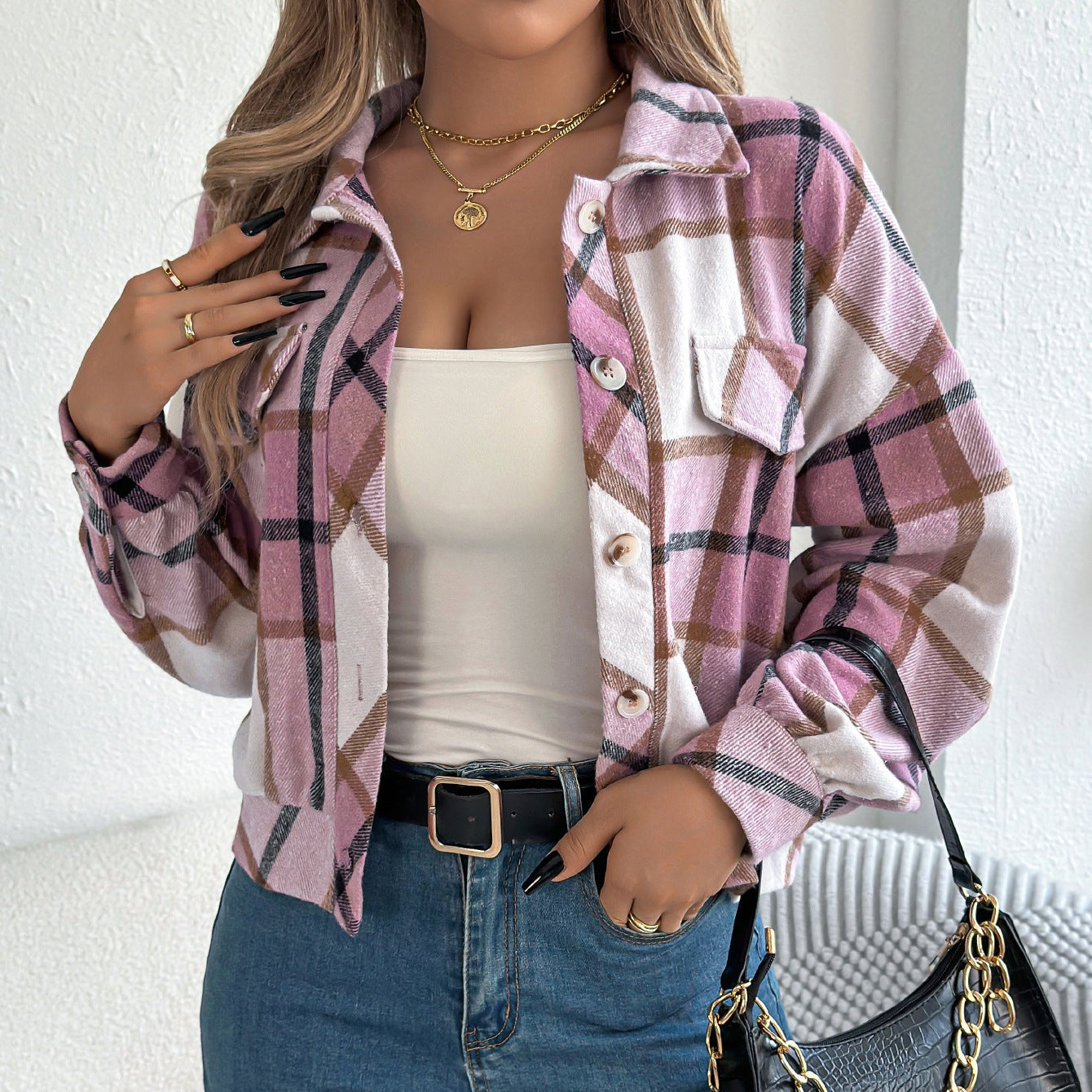 Donna con camicia a quadri rosa e bianca, top bianco, jeans blu, borsa nera. Moda casual autunnale, accessori eleganti, stile urbano.