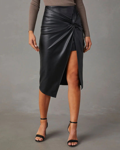 Gonna nera in ecopelle con spacco frontale, indossata con sandali neri e top a maniche lunghe marrone. Moda elegante e moderna.