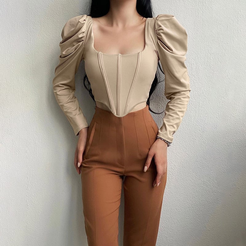 Donna in posa indossa top beige con maniche a sbuffo e pantaloni marroni. Moda elegante, abbigliamento femminile, stile contemporaneo.