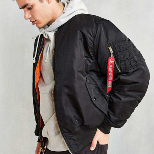 Giovane uomo con giacca bomber nera, felpa grigia con cappuccio, etichetta rossa su manica. Moda casual, abbigliamento streetwear uomo.