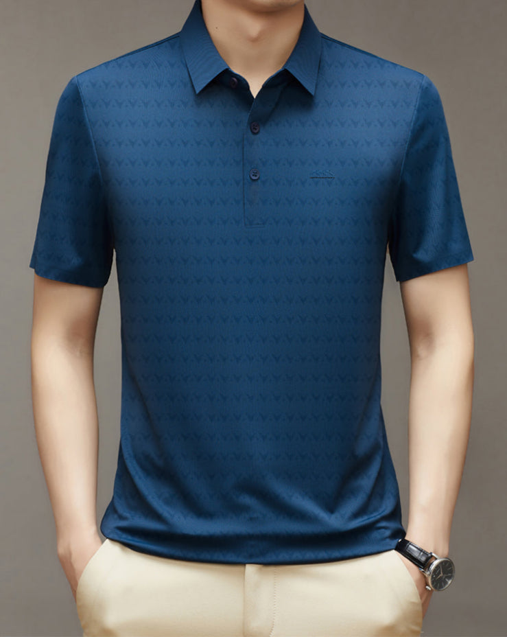 Camicia polo uomo blu scuro, motivo geometrico, maniche corte, abbinata a pantaloni beige. Stile casual elegante, moda maschile contemporanea.