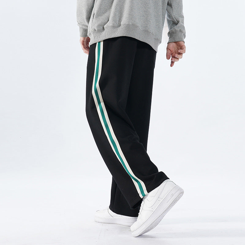 Uomo con pantaloni neri a righe verdi e bianche, felpa grigia e scarpe da ginnastica bianche. Moda casual, abbigliamento sportivo uomo.