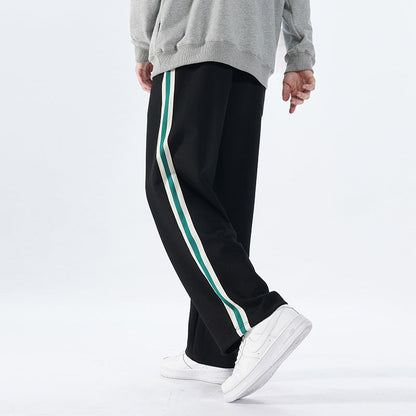 Uomo con pantaloni neri a righe verdi e bianche, felpa grigia e scarpe da ginnastica bianche. Moda casual, abbigliamento sportivo uomo.