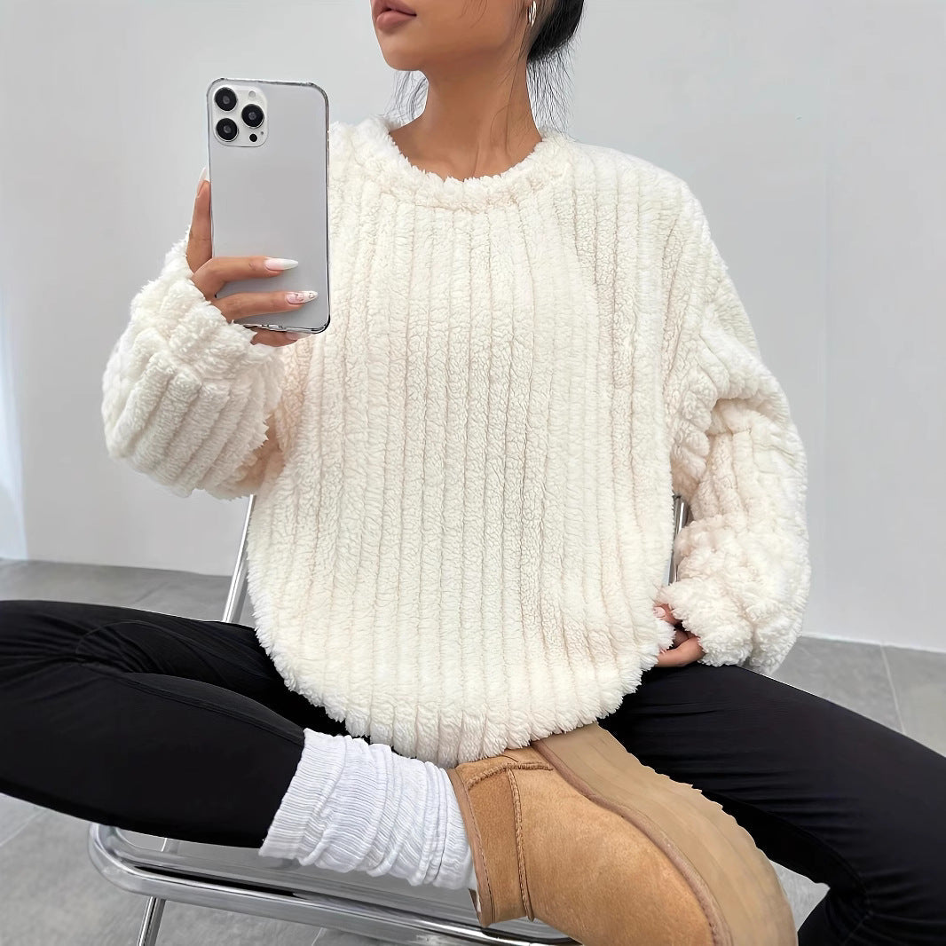 Donna seduta con maglione bianco in pelliccia sintetica, pantaloni neri, stivali beige e smartphone. Moda invernale casual, comfort e stile.
