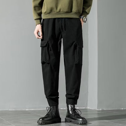 Pantaloni cargo neri da uomo, tasche laterali, abbinati a stivali neri e maglione verde. Stile casual moderno, moda maschile autunnale.
