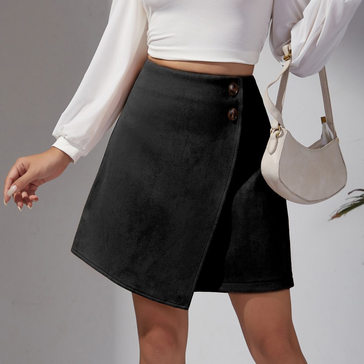 Donna con gonna nera a portafoglio e bottoni, top bianco a maniche lunghe, borsa beige. Moda femminile elegante e moderna.